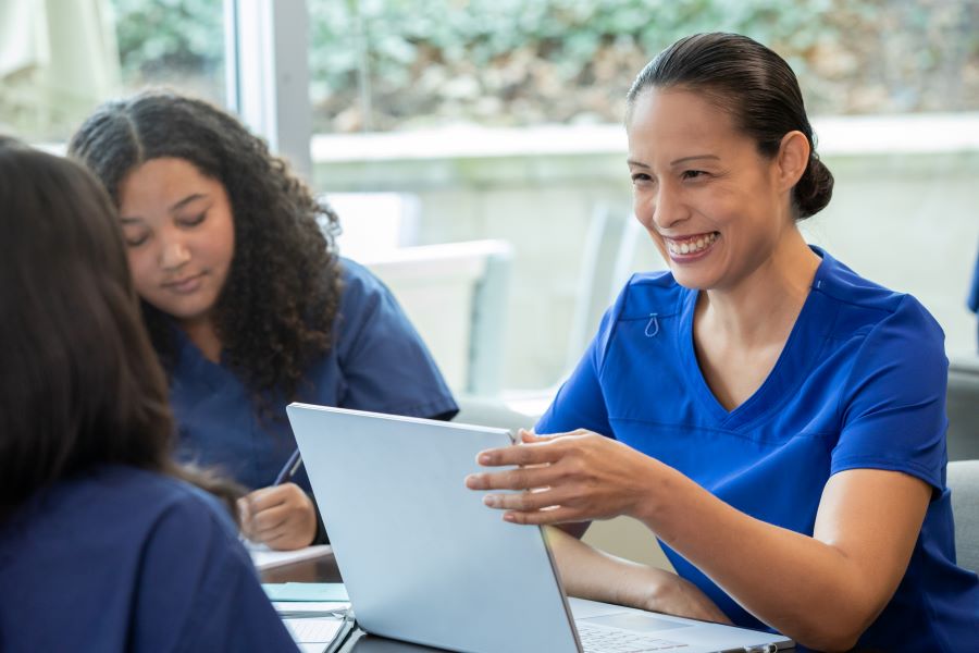 Women health workers dressed in blue sitting at a table with a computer
