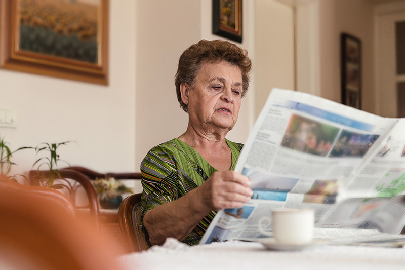 older woman at a table reading the paper