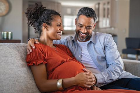 A pregnant woman on a couch with a man touching her stomach