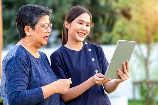Young person holding a tablet while an older person looks on.