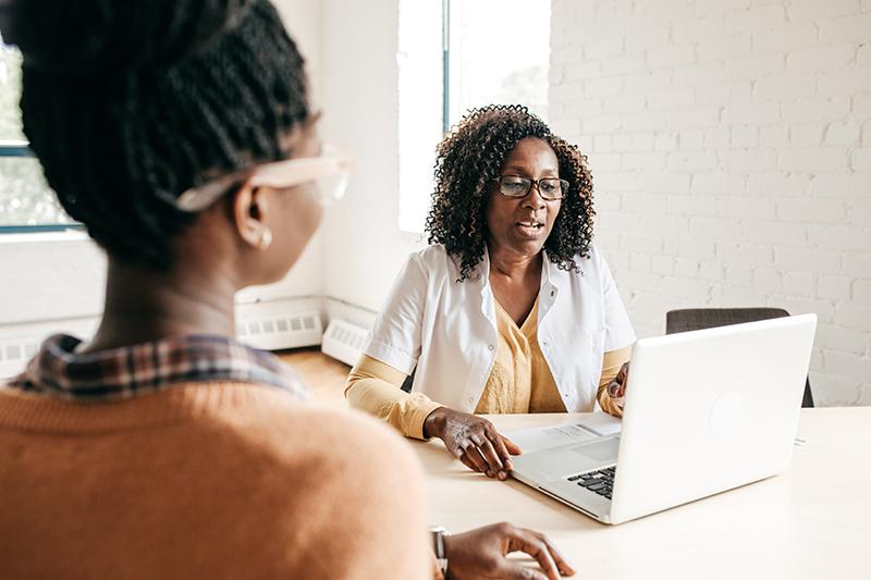 Two women talking at a desk with a computer